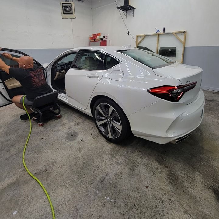 A white car with open door in a garage, a person installing window tint.