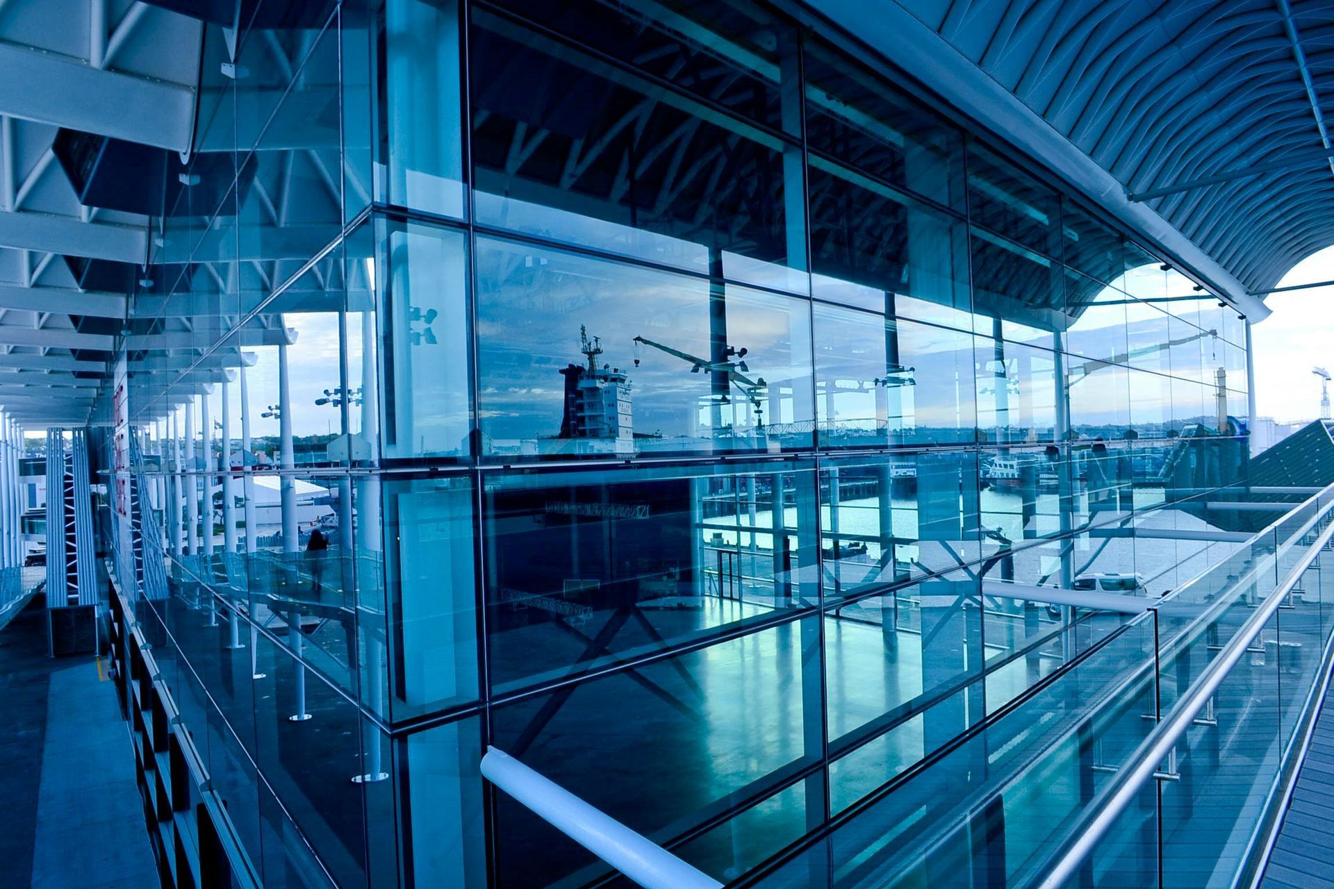 Modern glass building with reflections of sky and surrounding area. Blue tones.