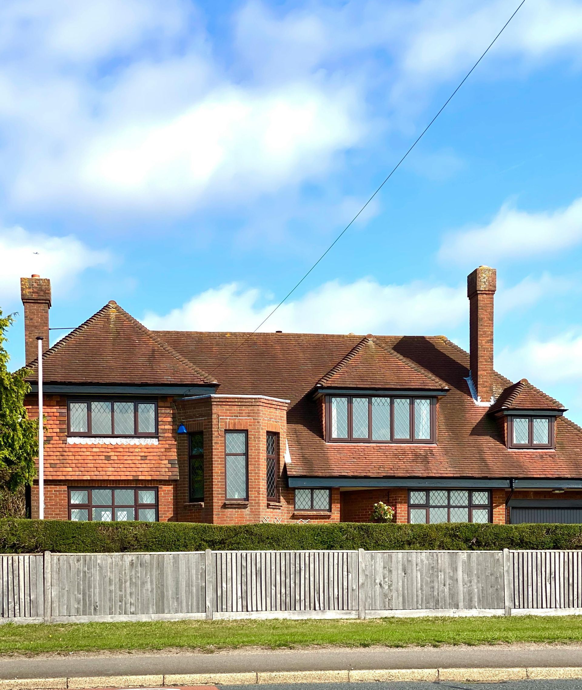Brick house with brown tile roof, wooden fence, blue sky with clouds, and birds in flight.