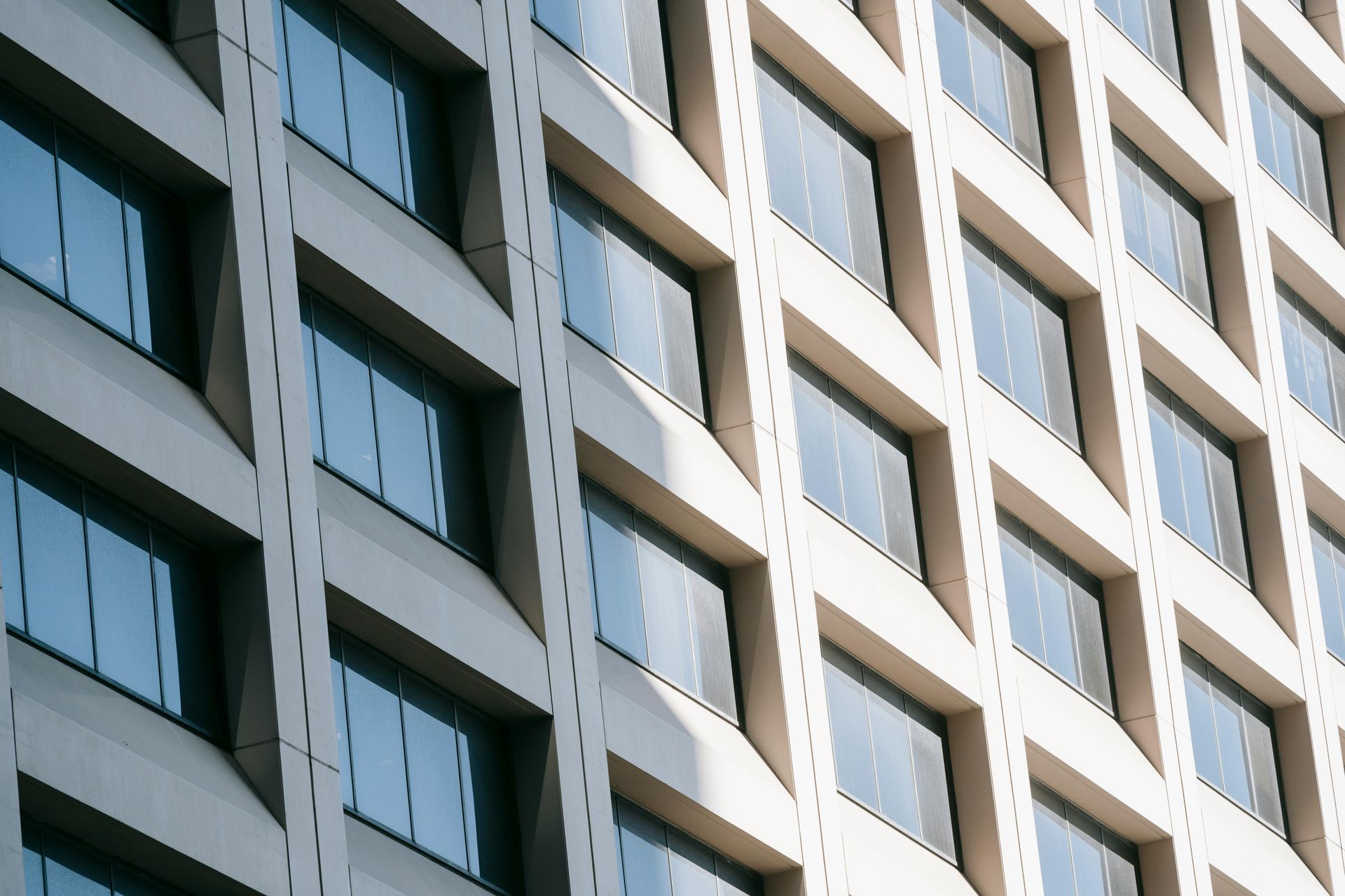 Modern building exterior with rows of rectangular windows, bright sunlight.