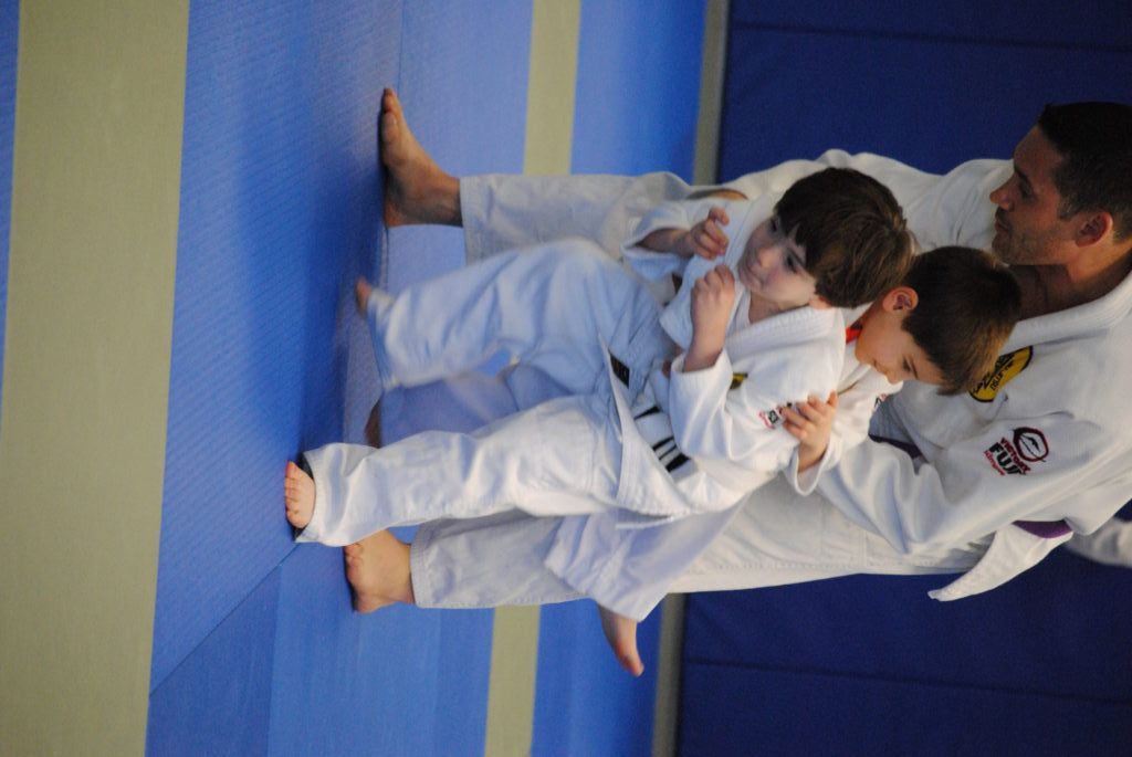 A man and two children are practicing judo on a blue mat.