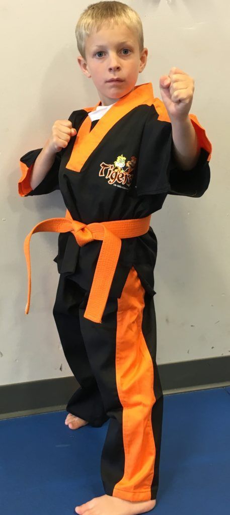 A young boy in a black and orange karate uniform is standing on a blue mat.