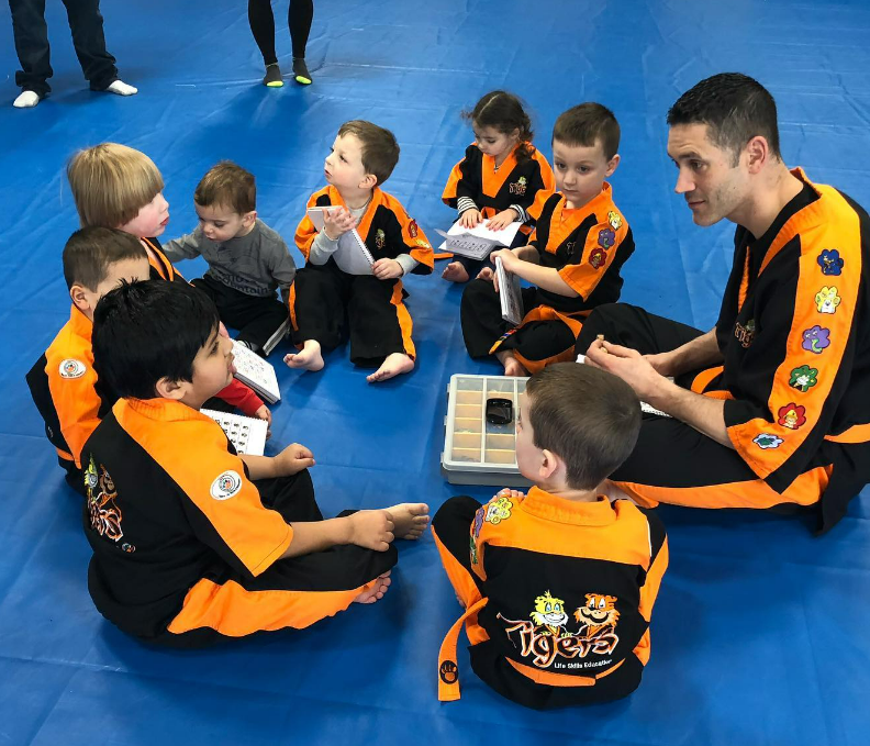 A young boy in a black and orange karate uniform is standing on a blue mat.