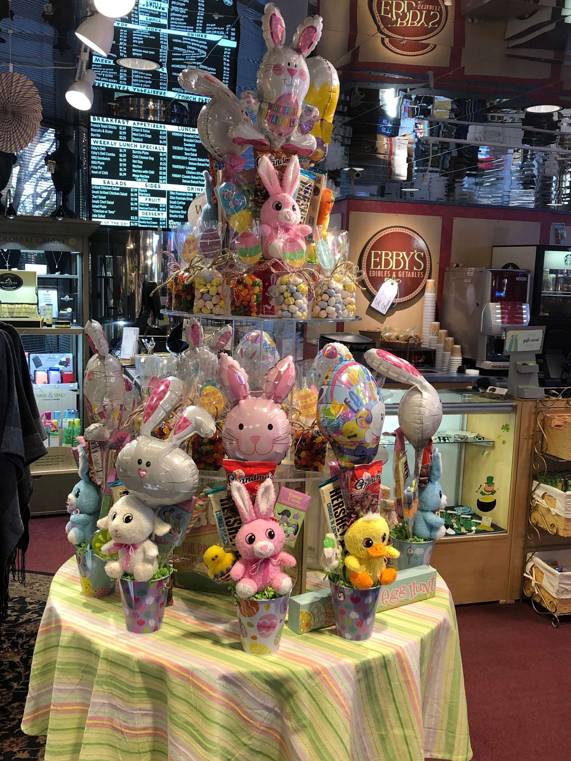 Table of pastel Easter bunny and chick plush toys in a shop display, with larger bunnies stacked behind them.