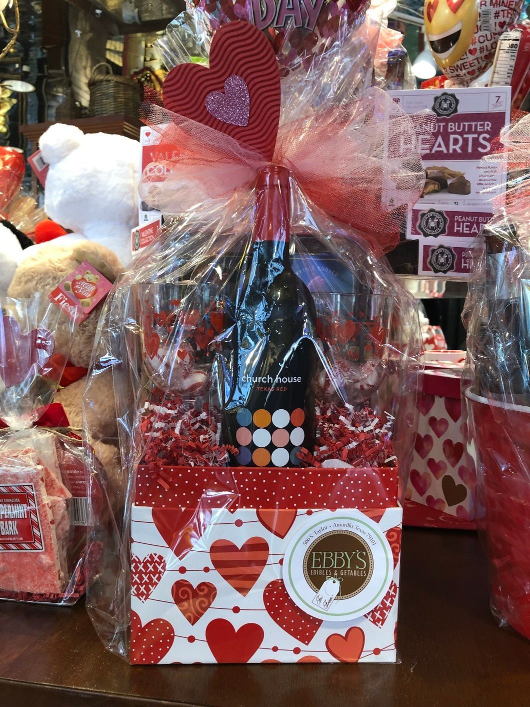 Gift basket with red hearts, ribbon, and chocolates displayed in a shop window.