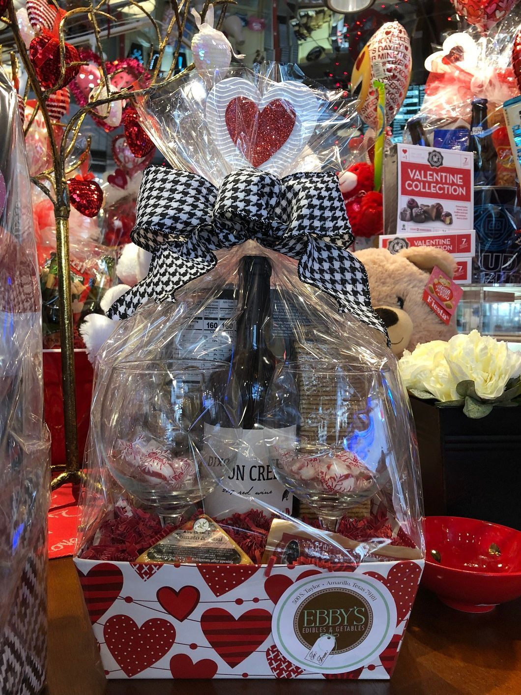 Heart-themed gift basket with red and white decorations, a big bow, and wrapped items in a festive display.