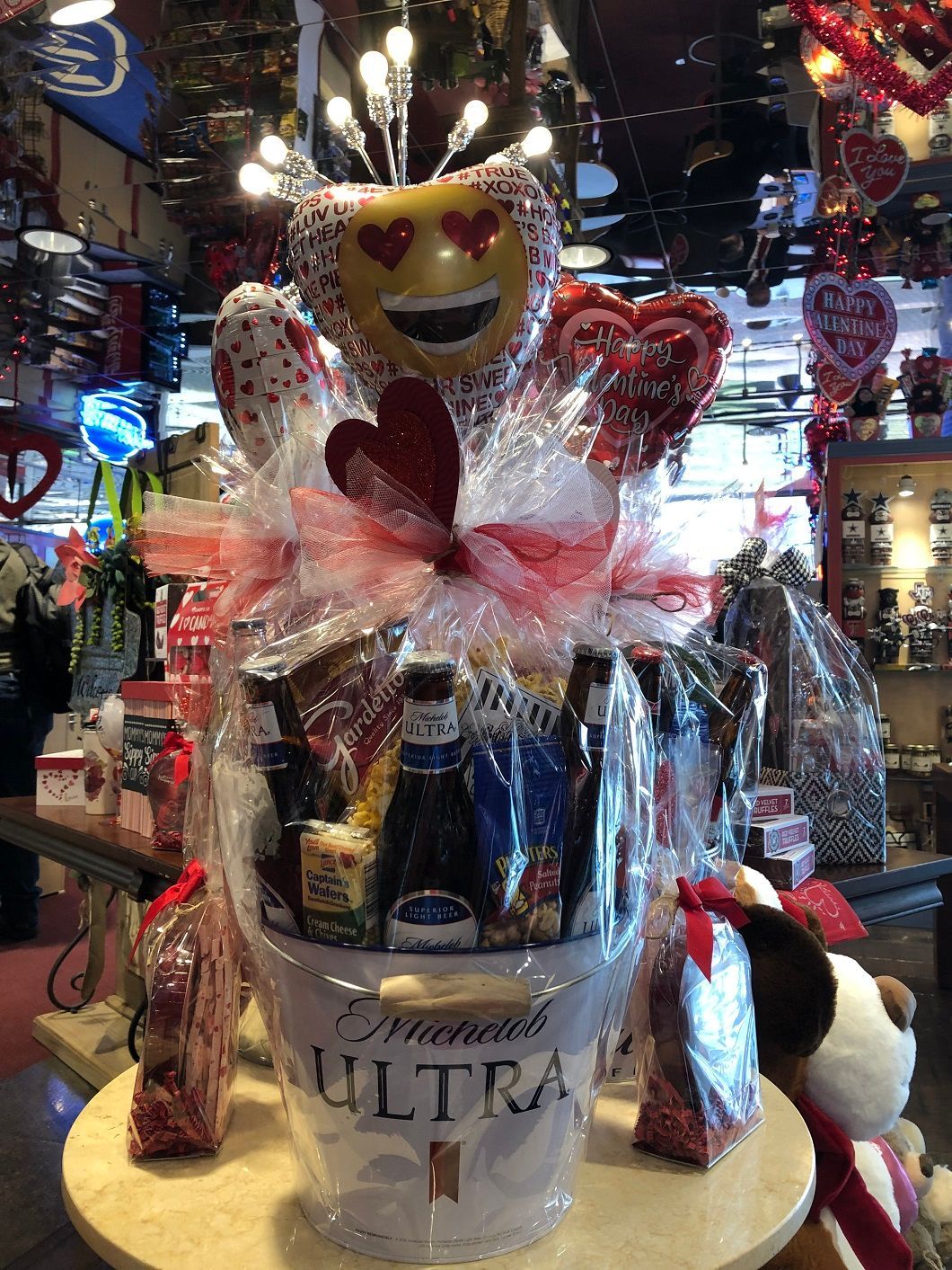 Gift basket with beer and Valentine decorations, featuring a smiling heart and red ribbons in a store display