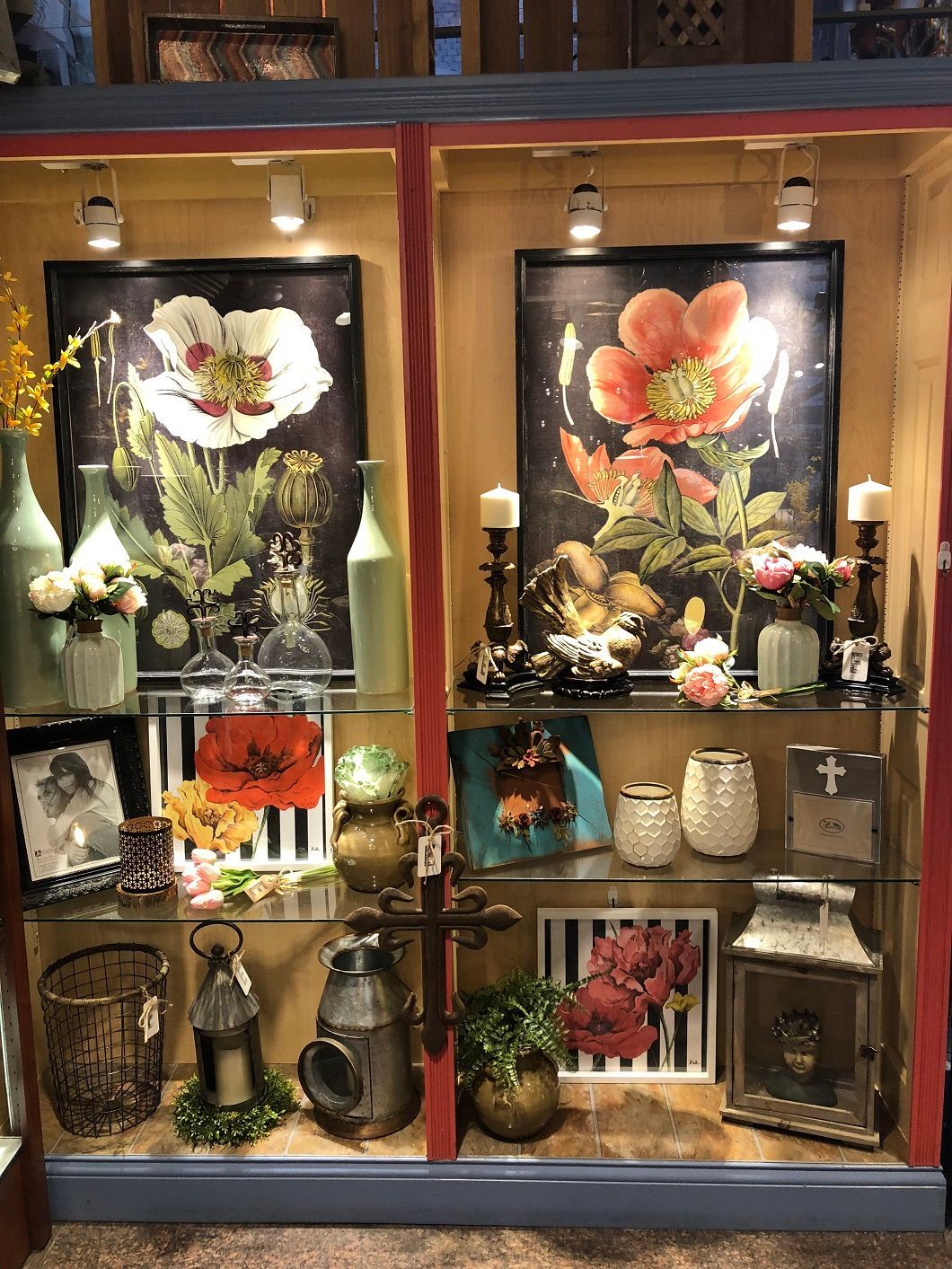 Decorative display cabinet with framed flower art, candles, vases, and small ornaments on glass shelves