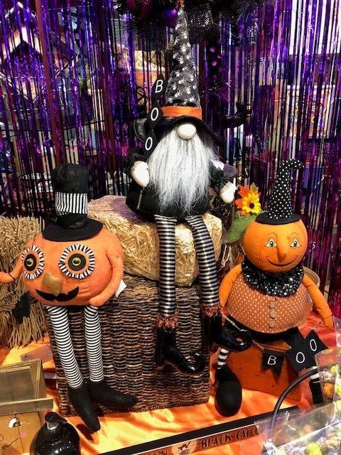 Three Halloween gnome figurines with pumpkin heads on a purple tinsel backdrop