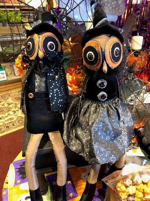 Two spooky black cat dolls in a shop display, one in a black dress and one in a silver skirt.