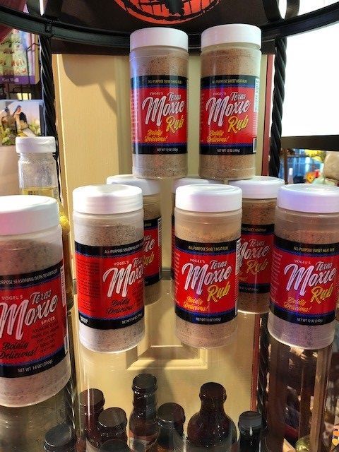 Display of red-labeled product containers on a shelf, with brown bottles below and a plant in the background