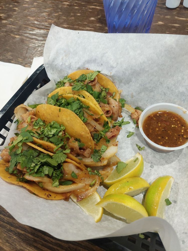 Taco platter with cilantro, onions, lime wedges, and salsa on a tray lined with paper.