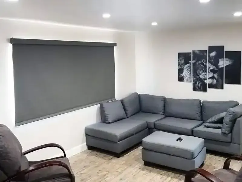 A living room with a sectional couch , chairs , ottoman and a large window.