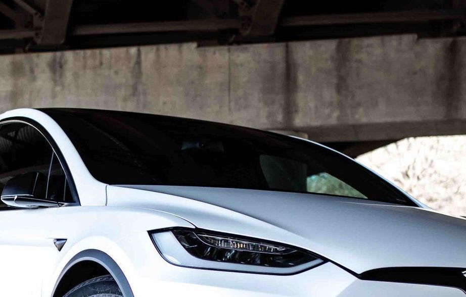 White Tesla X SUV under a concrete overpass.