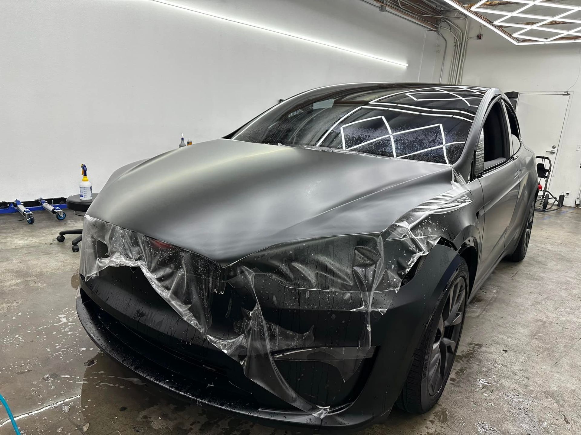 Damaged black sedan with a crumpled hood and shattered front end in a garage