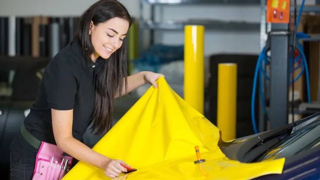A woman is wrapping a car with yellow vinyl.