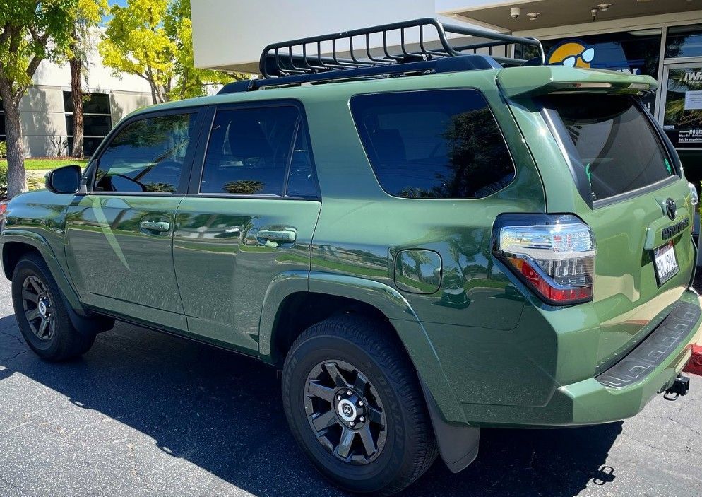 Green SUV parked on a street, viewed from the rear side, with roof rack and black wheels