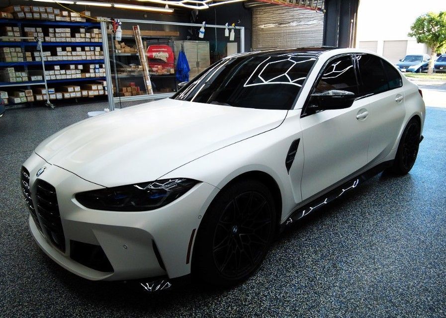 White BMW sedan with black accents parked on a gray-speckled floor, possibly a shop.