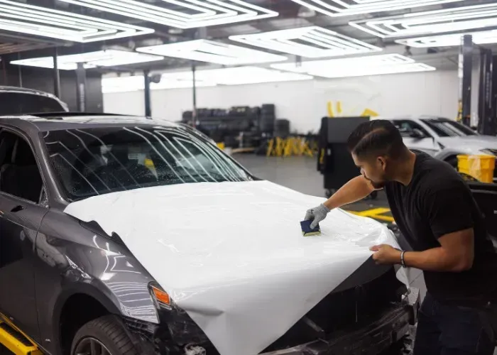 A man is wrapping the hood of a car in a garage.