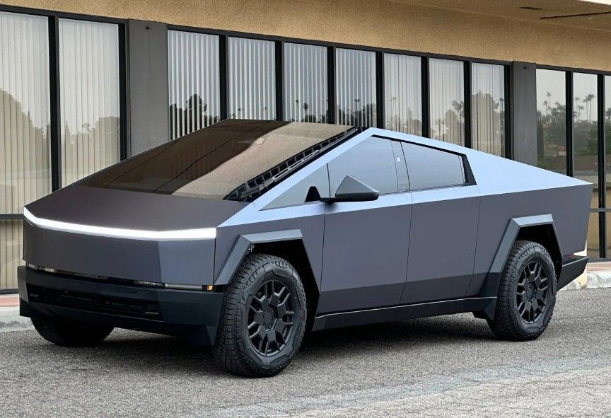 Angular silver Tesla Cybertruck parked outside a glass-front building.