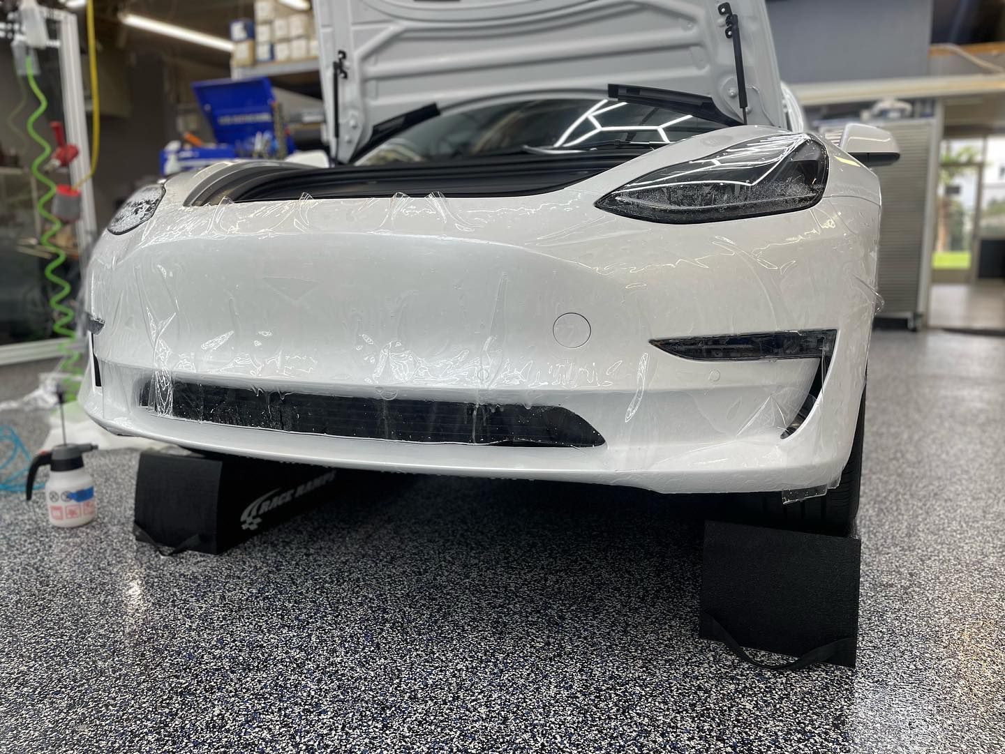 White Tesla being covered in protective film in a garage.