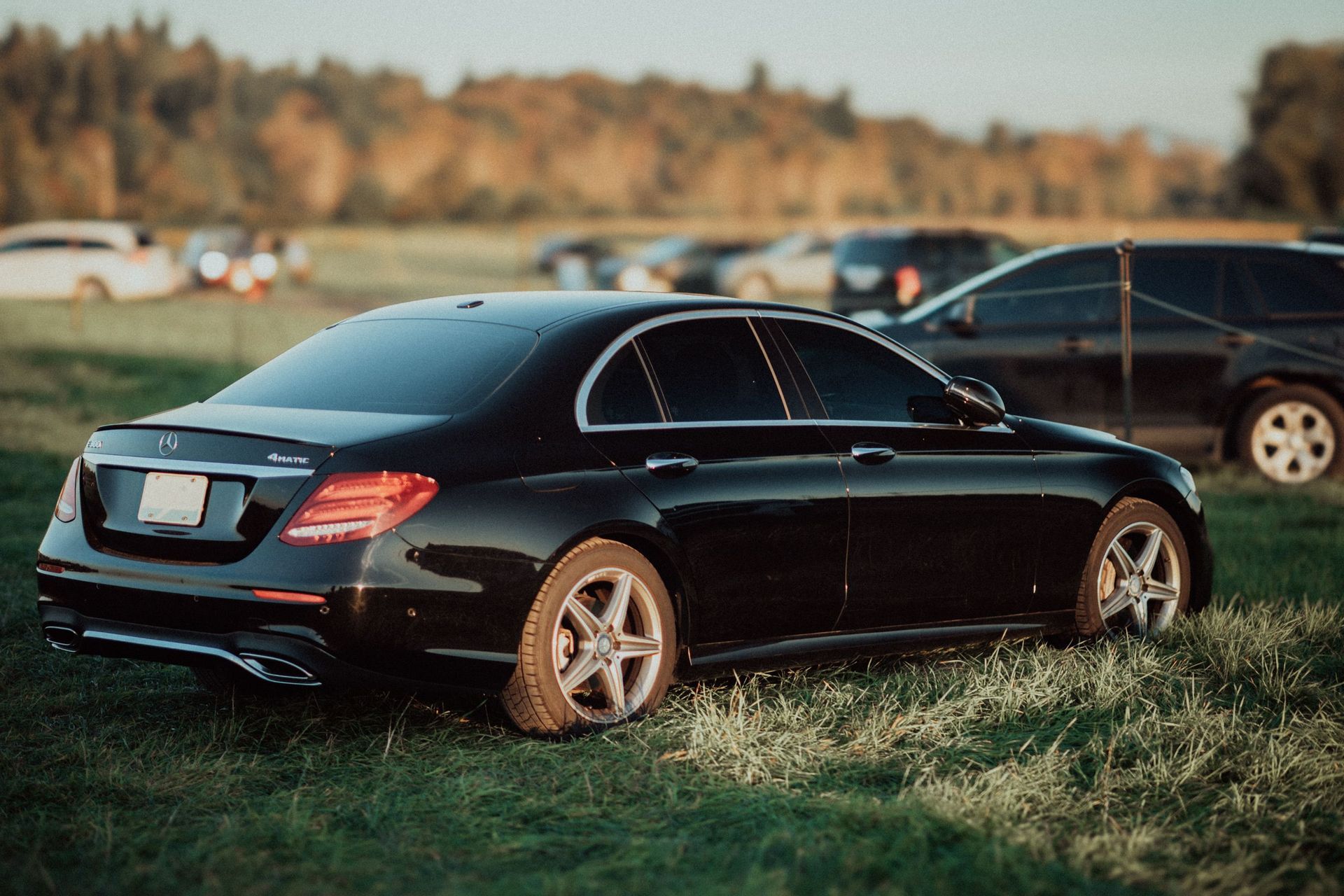 Black Mercedes sedan parked on grass at an outdoor event, with other cars in the background
