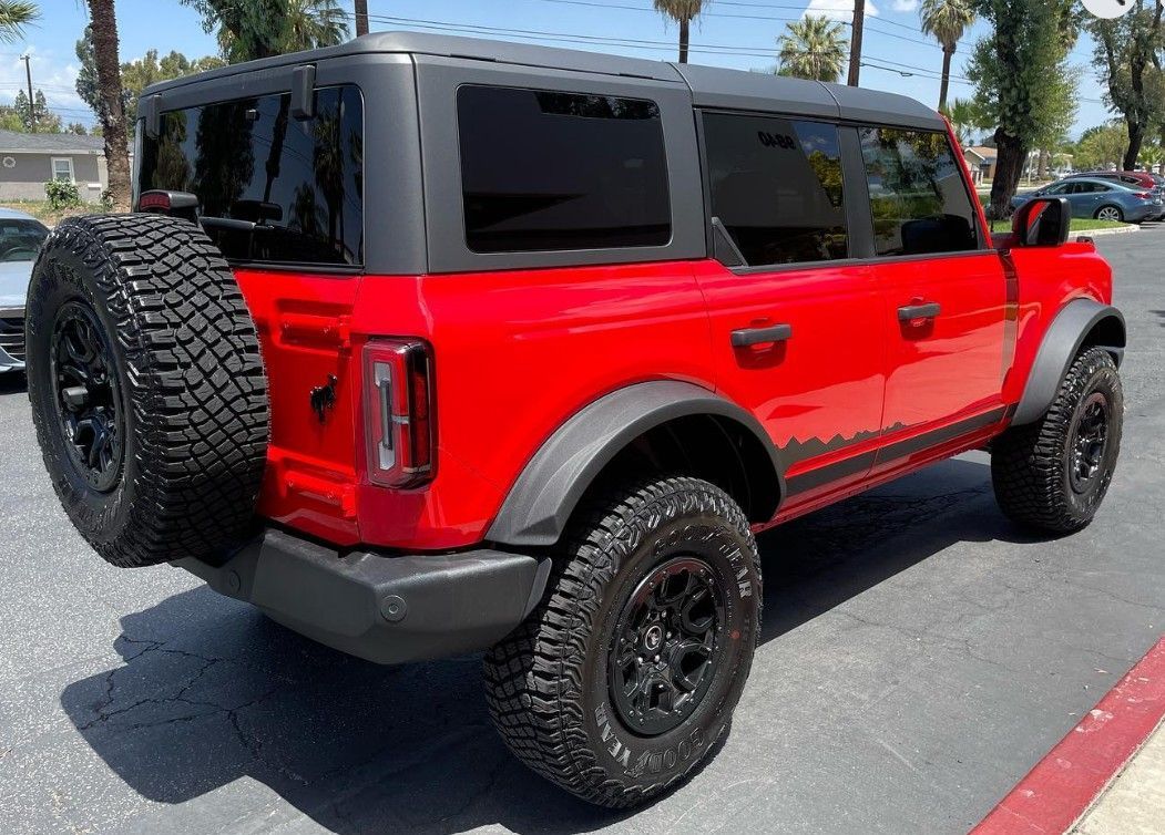 Red off-road SUV with black roof and spare tire parked in a sunny lot.