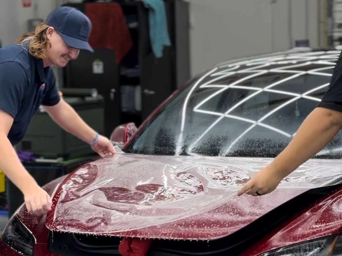 A man is cleaning a red car with a blue sponge