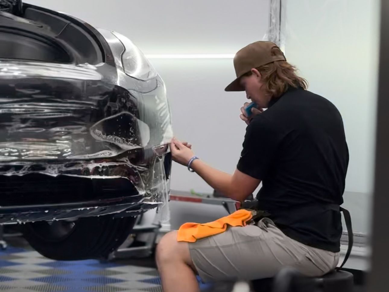 A man wearing a hat is cleaning the hood of a car