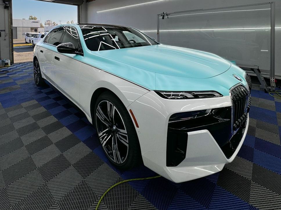 A white car with a blue wrap is parked in a garage.