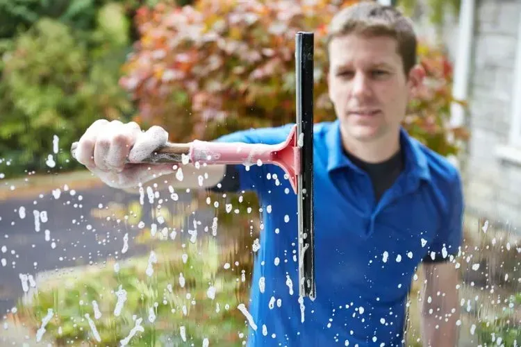 A man in a blue shirt is cleaning a window with a squeegee.