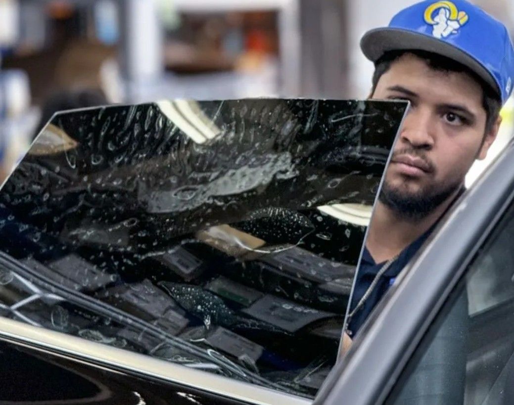 Car wash worker in blue cap washing a car window with a squeegee, reflecting lights and equipment