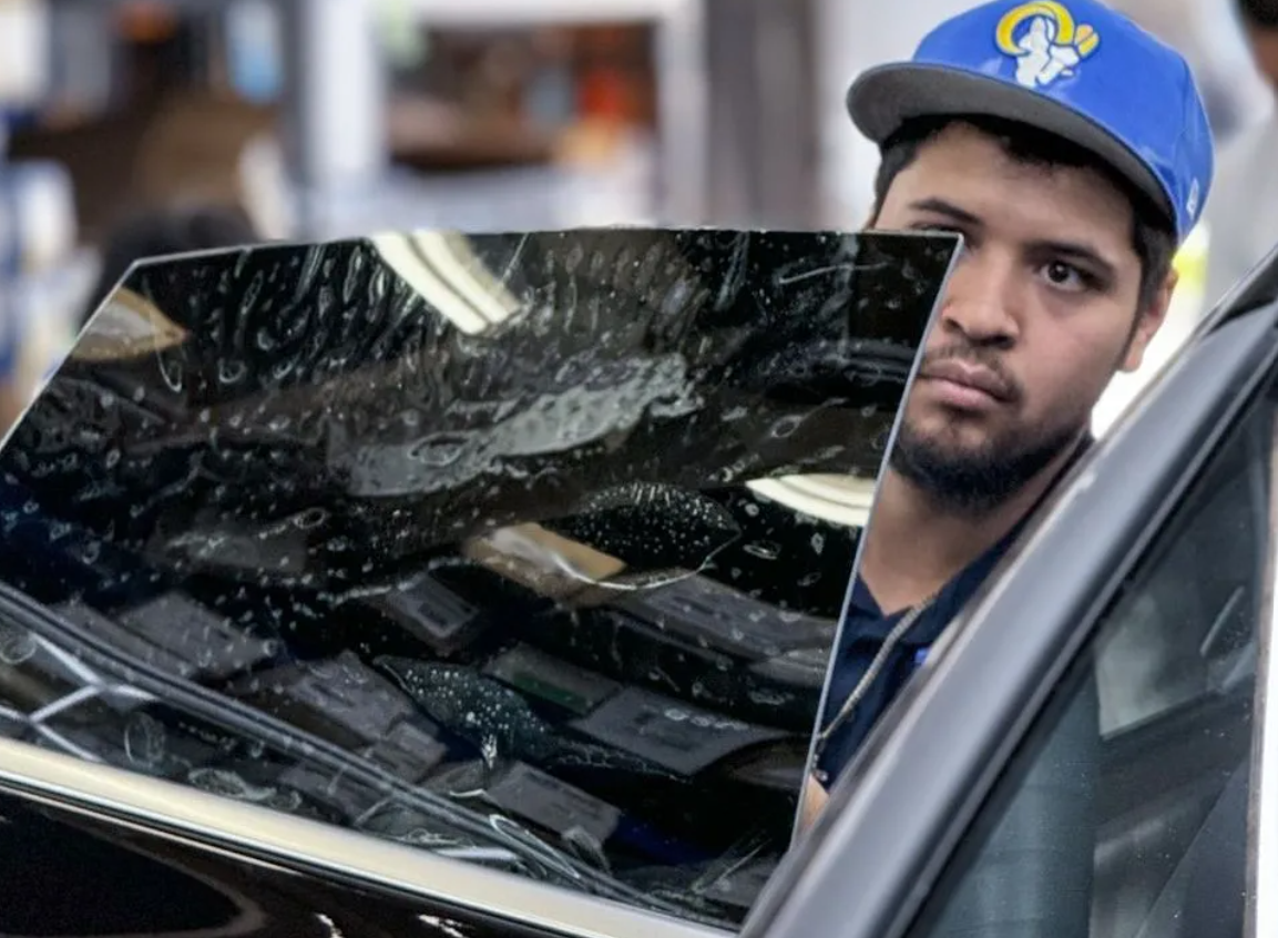 Man in a blue cap peeks over a car door with a scratched windshield