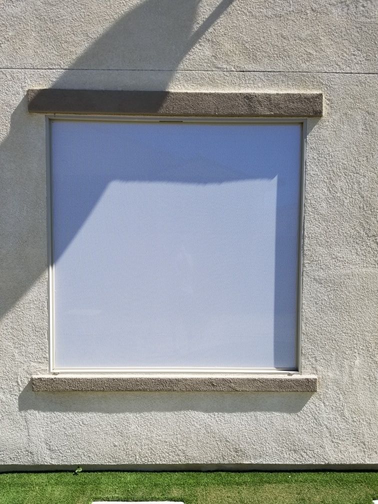 A square window on the side of a building with a shadow on it.