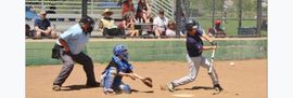 Baseball glove with ball on green grass, with blurred baseballs in the background.