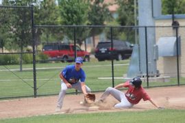 Baseball player sliding into home plate, catcher in front. Blue and gold uniforms, action shot.