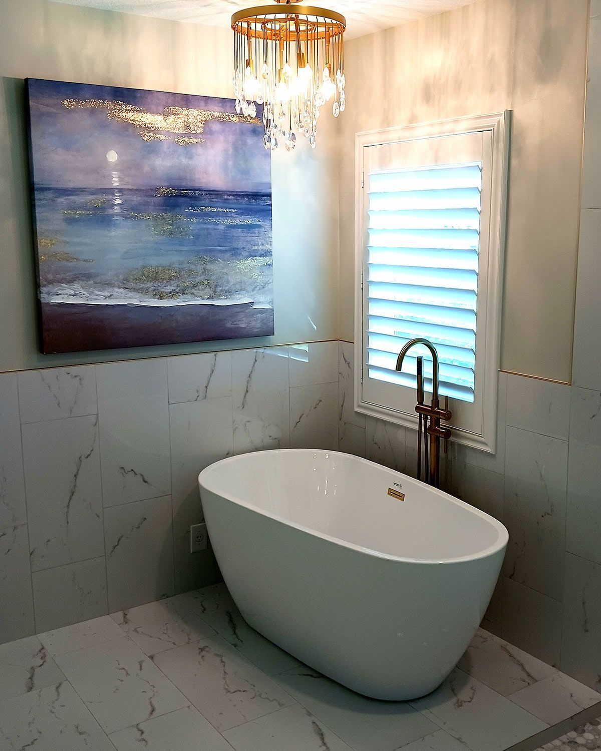 Modern bathroom with a freestanding white tub, rain shower, window blinds, and ocean painting