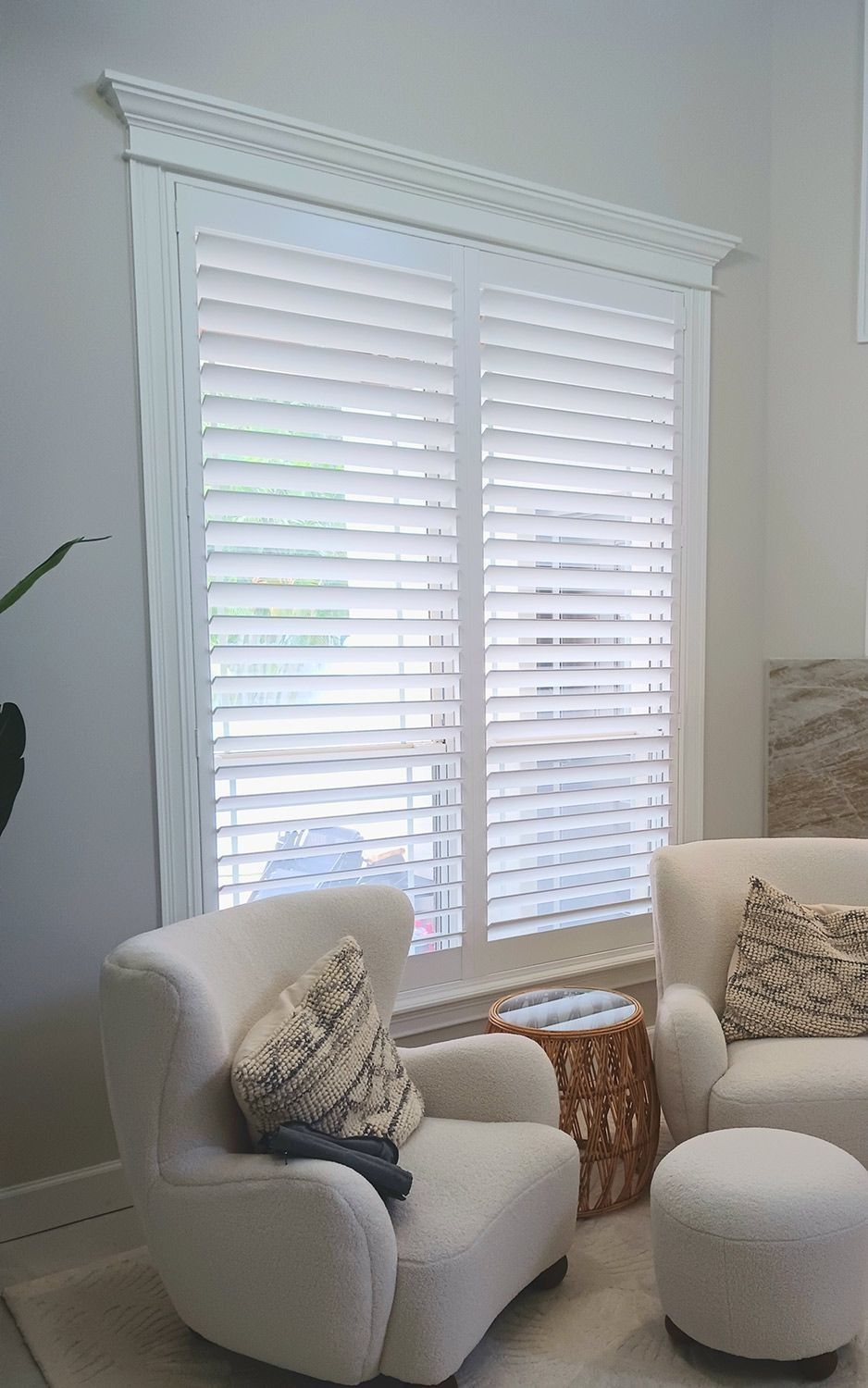 Bright living room with white shutters, cream armchair, ottoman, and patterned pillows