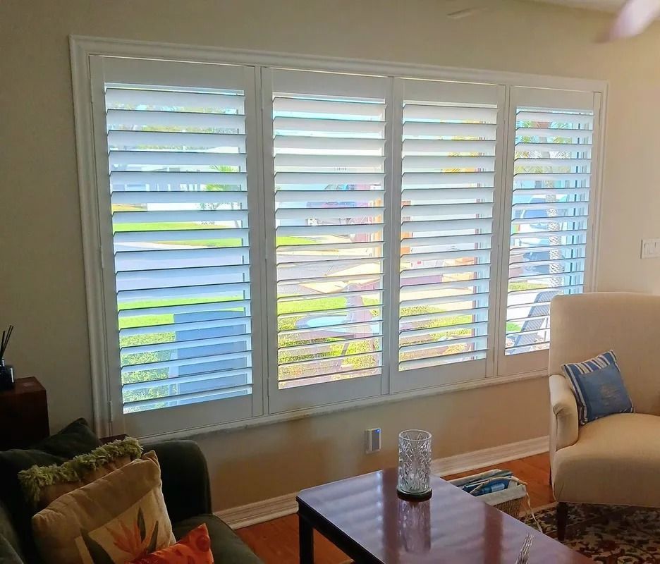 Living room with white plantation shutters, sunlight streaming in, sofa, coffee table, and orange chair