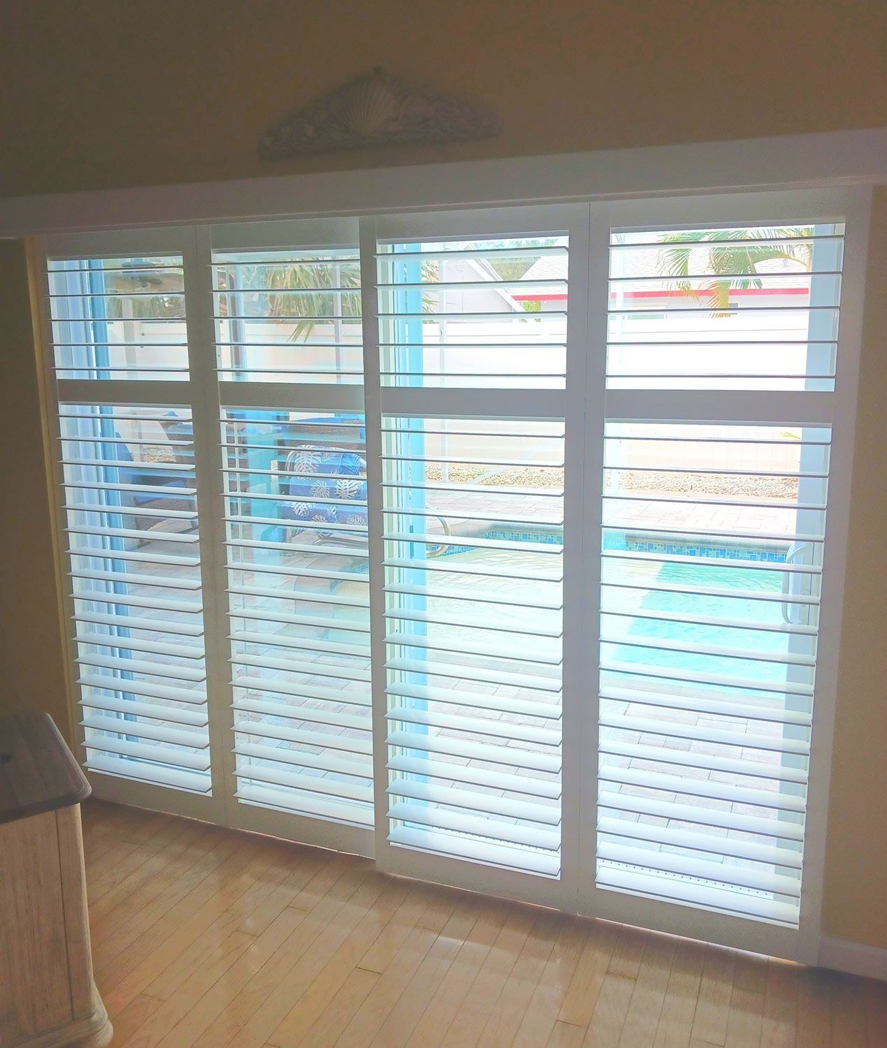 Large white plantation shutters covering a glass sliding door in a bright room with wood floors.