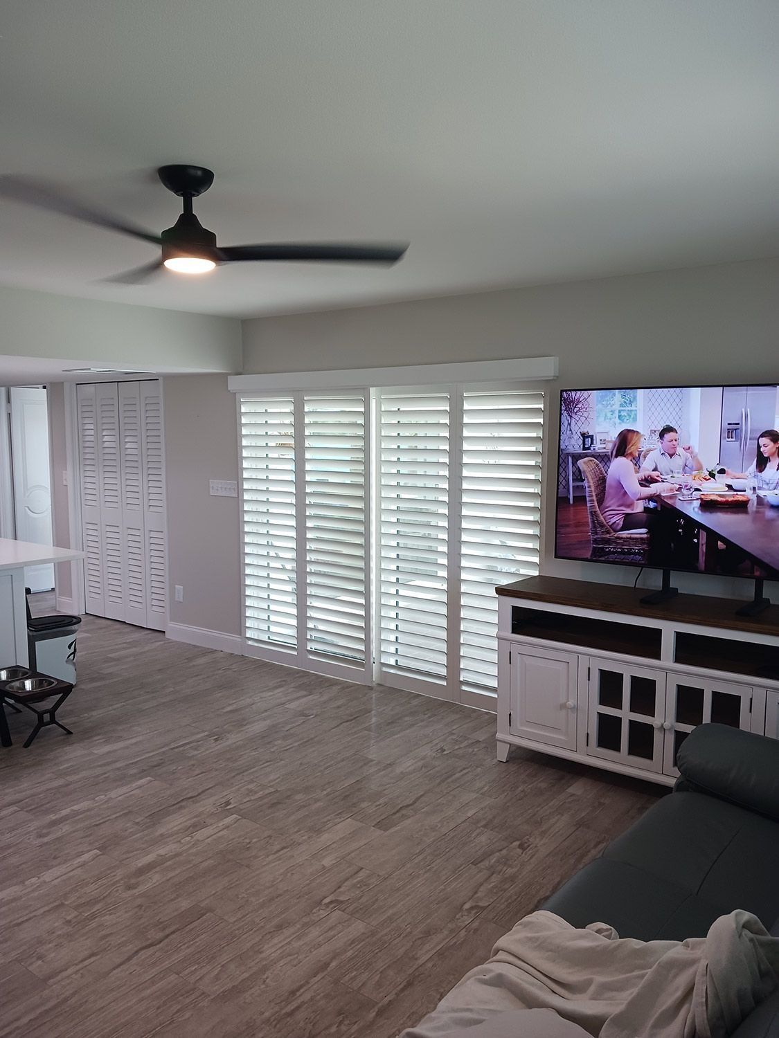 Bright living room with ceiling fan, white shutters, TV, and a sofa on wood flooring