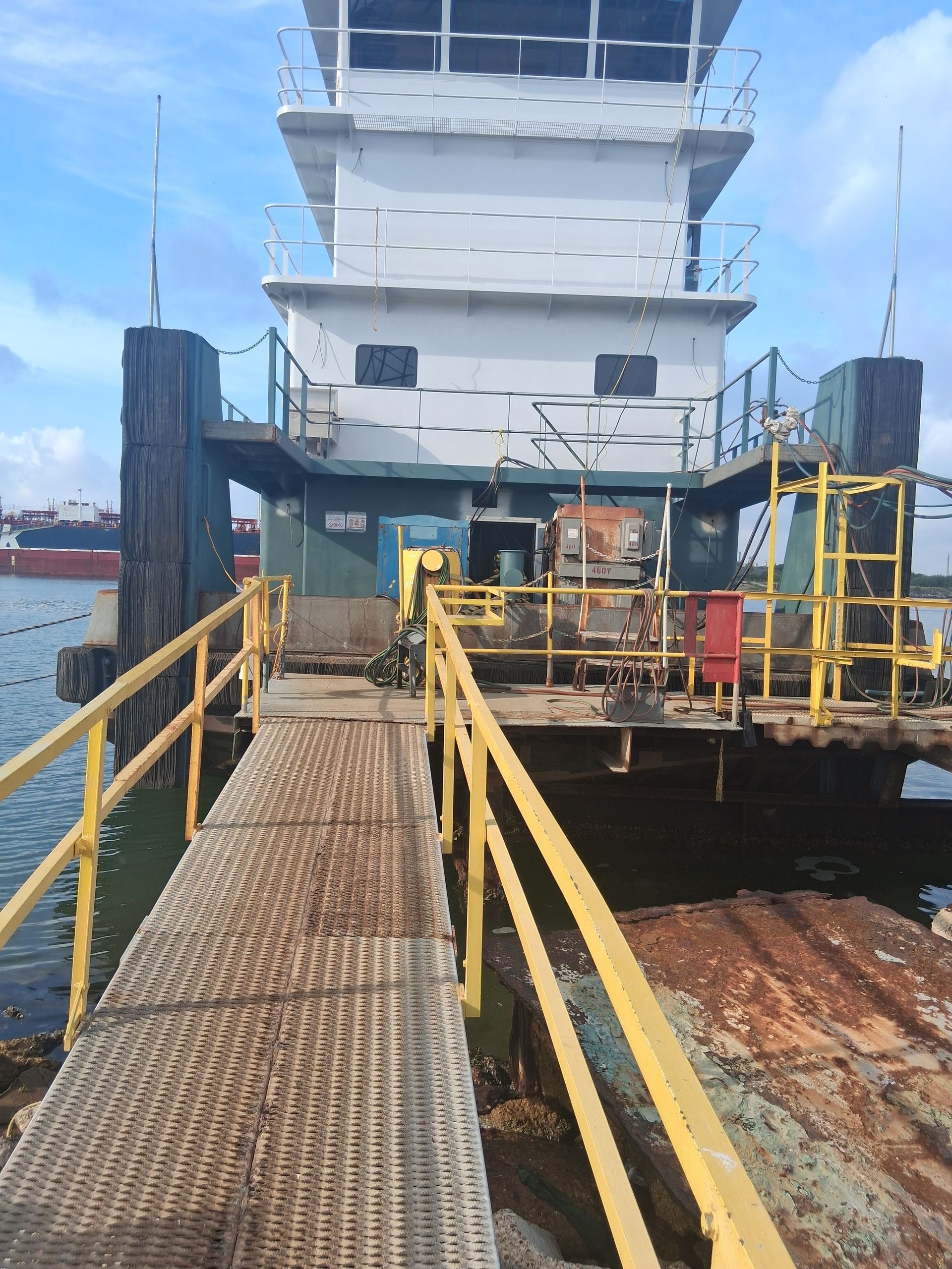 Rusted dock ramp leading to a large white ship with yellow railings and equipment on the deck