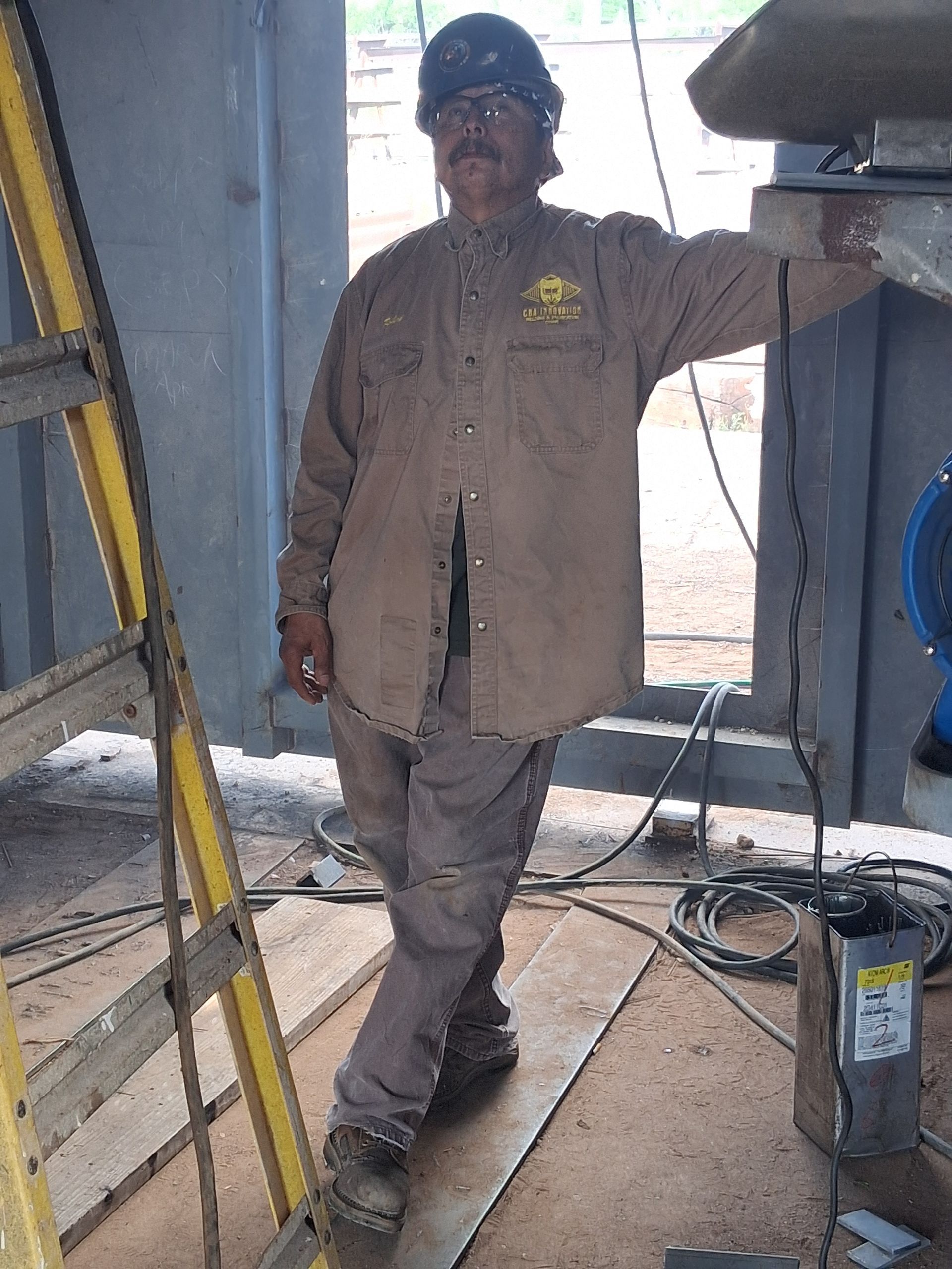 Worker in a hard hat leaning in an industrial doorway beside a ladder and tools.
