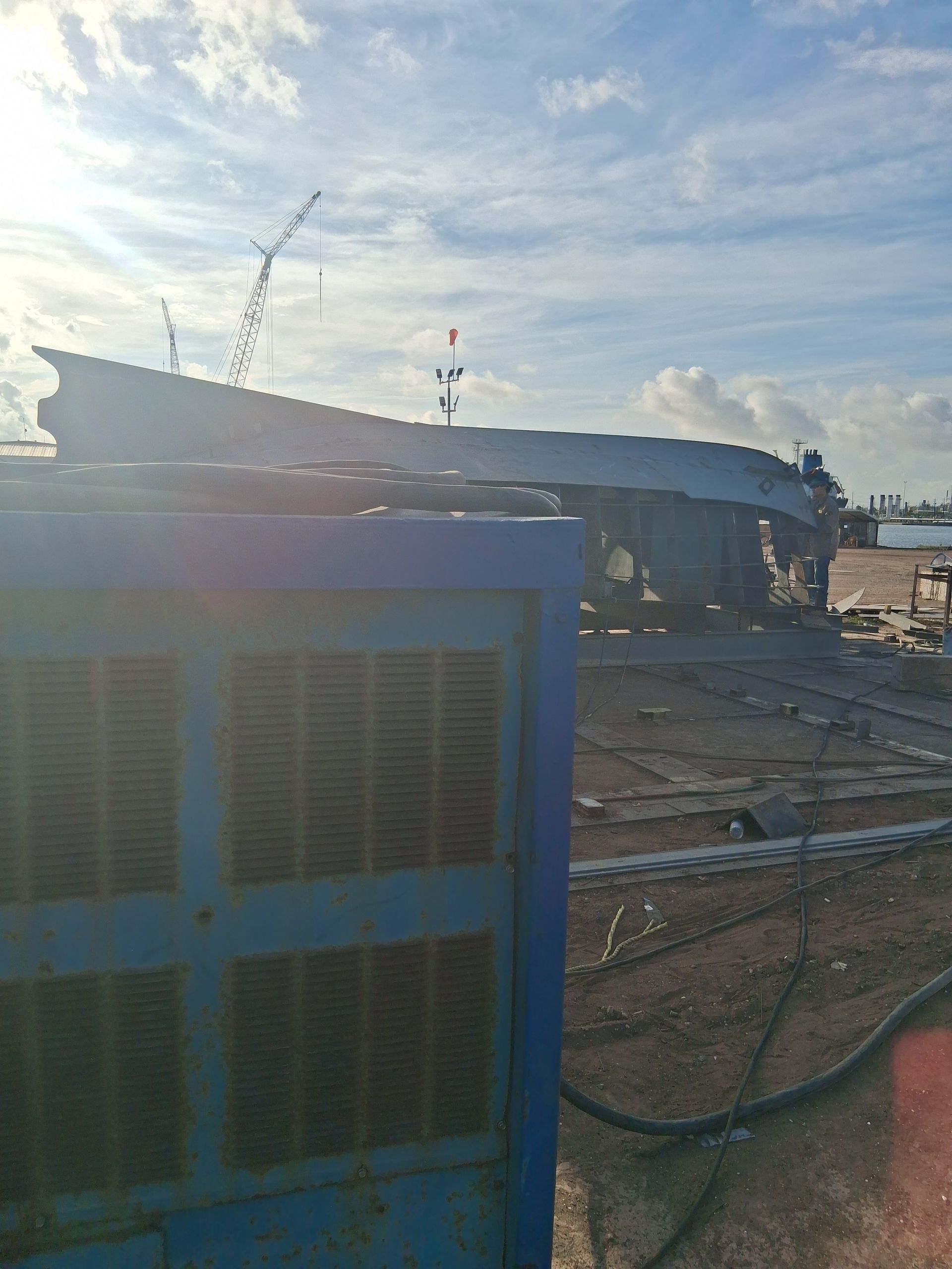 Blue industrial machine on a dusty construction site at sunset with damaged structure in the background