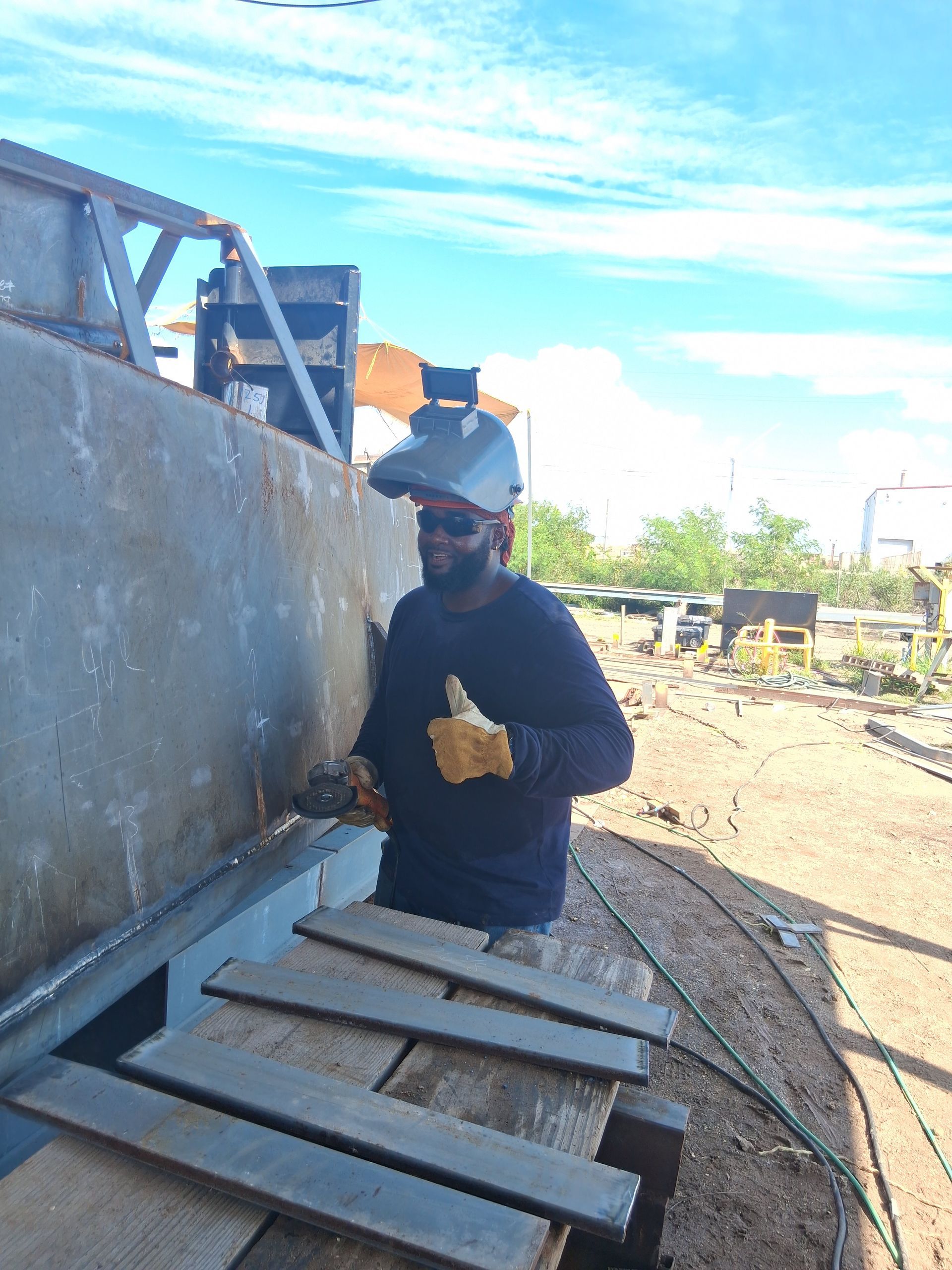 Worker in hard hat inspecting a large industrial tank outdoors, with metal grating in the foreground.