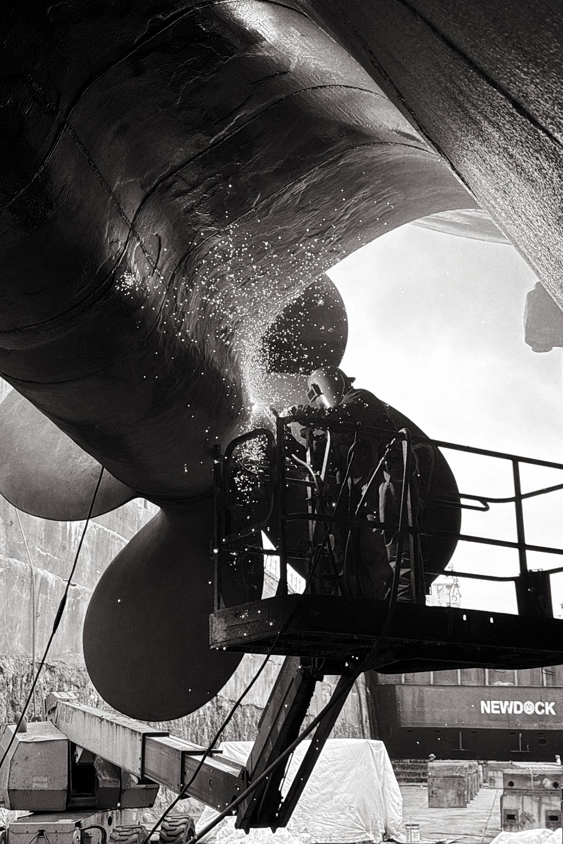 Crew working on a large ship propeller and shaft in a shipyard, black-and-white photo