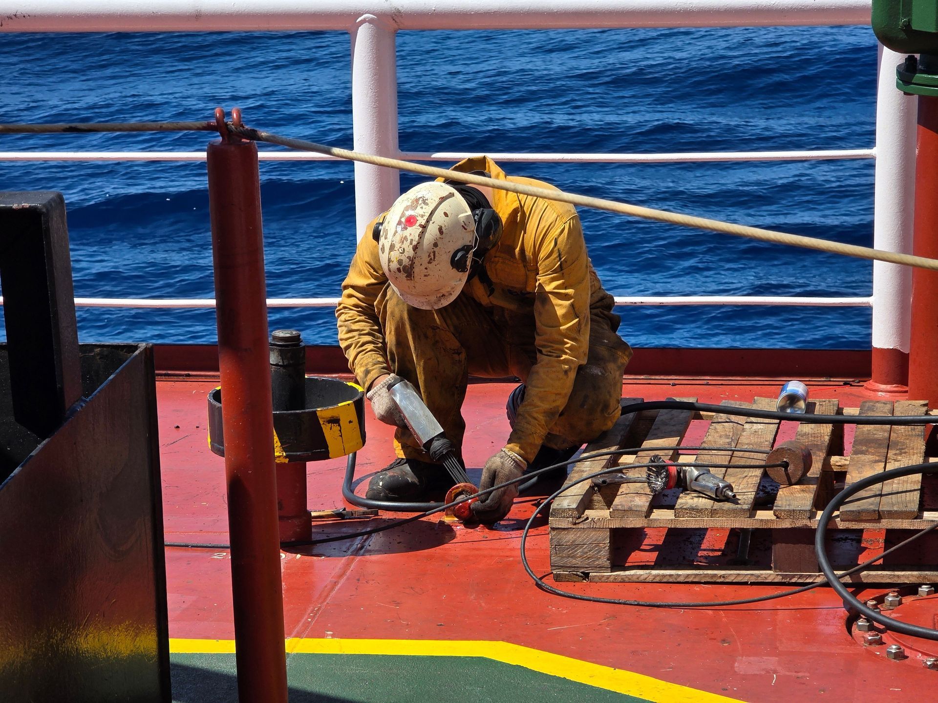 Worker in yellow gear welding on a ship deck beside the ocean.