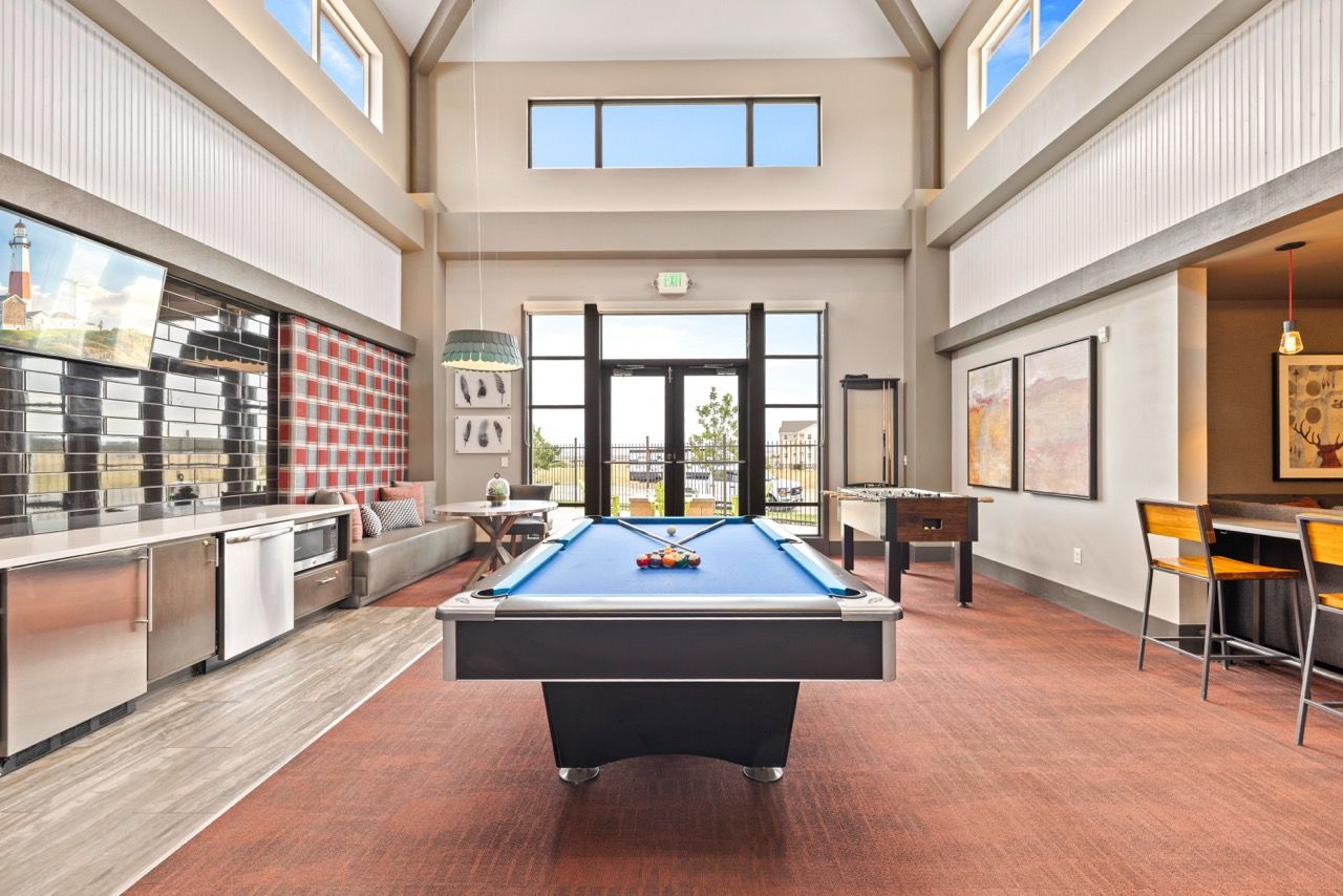Clubhouse recreation room with a blue pool table, foosball, lounge seating, and a kitchenette.
