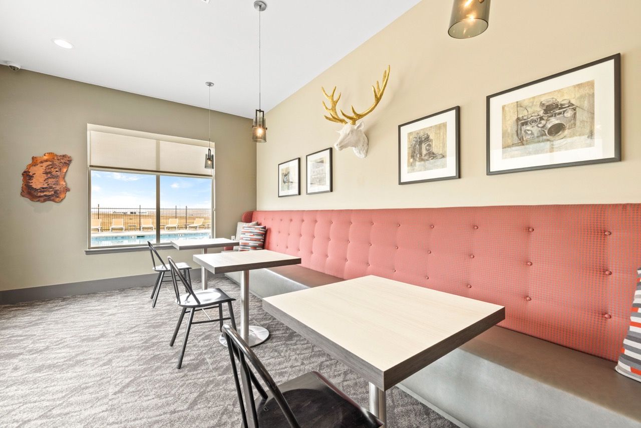 Indoor community lounge with pink tufted banquette, small tables, and wall art.