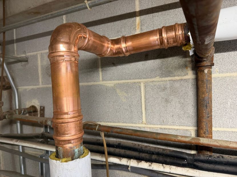 Copper plumbing pipes and elbows against a cinderblock wall in a basement utility area